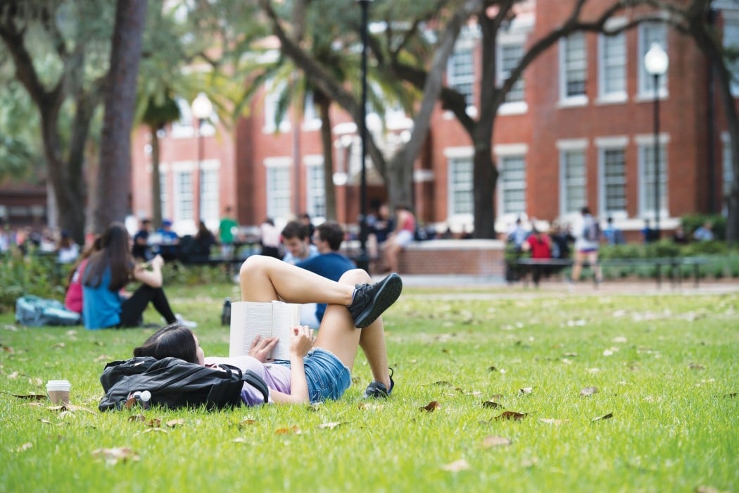student reads book in the grass in the plaza
