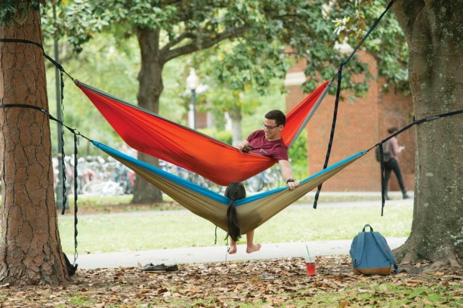 two students enjoying resting in hammock that are hung from large oak trees in the Plaza of the Americas