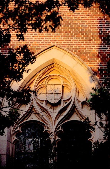 large stained-glass window in Dauer Hall, constructed in collegiate Gothic architecture featuring plaster bas reliefs depicting the sun, trees, boats and native Americans
